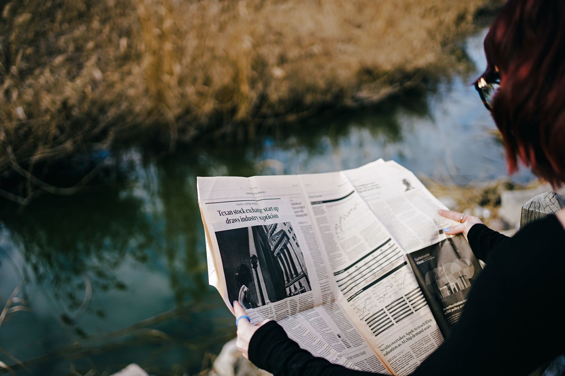 A person enjoys reading a newspaper by a tranquil pond on a sunny day. — How Sports Toto Broadcasts Improve Sports Viewing Ex