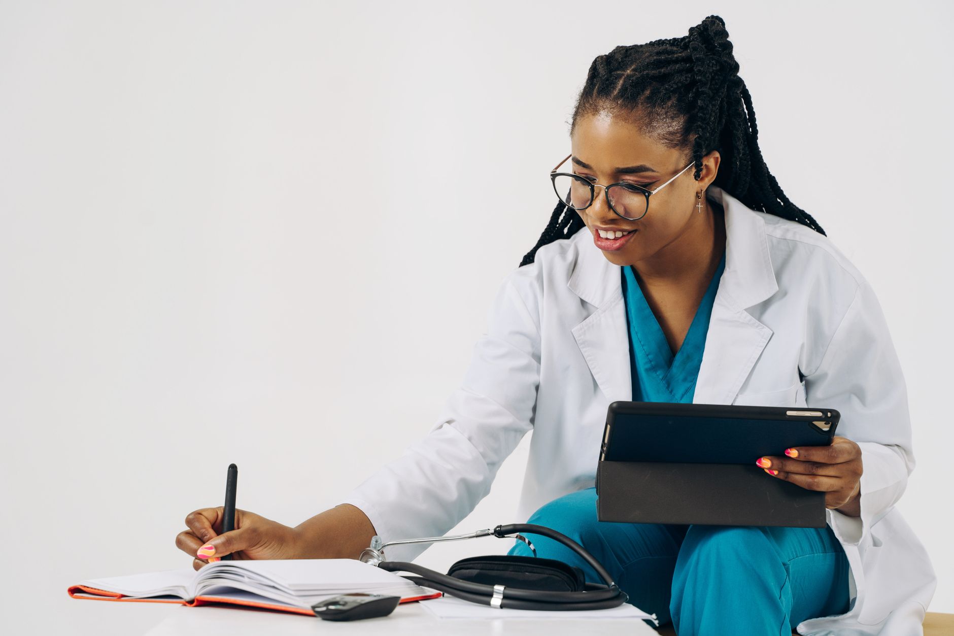 Smiling female doctor in scrubs using tablet and taking notes in a healthcare setting. — Innovative Healthcare Solutions by E