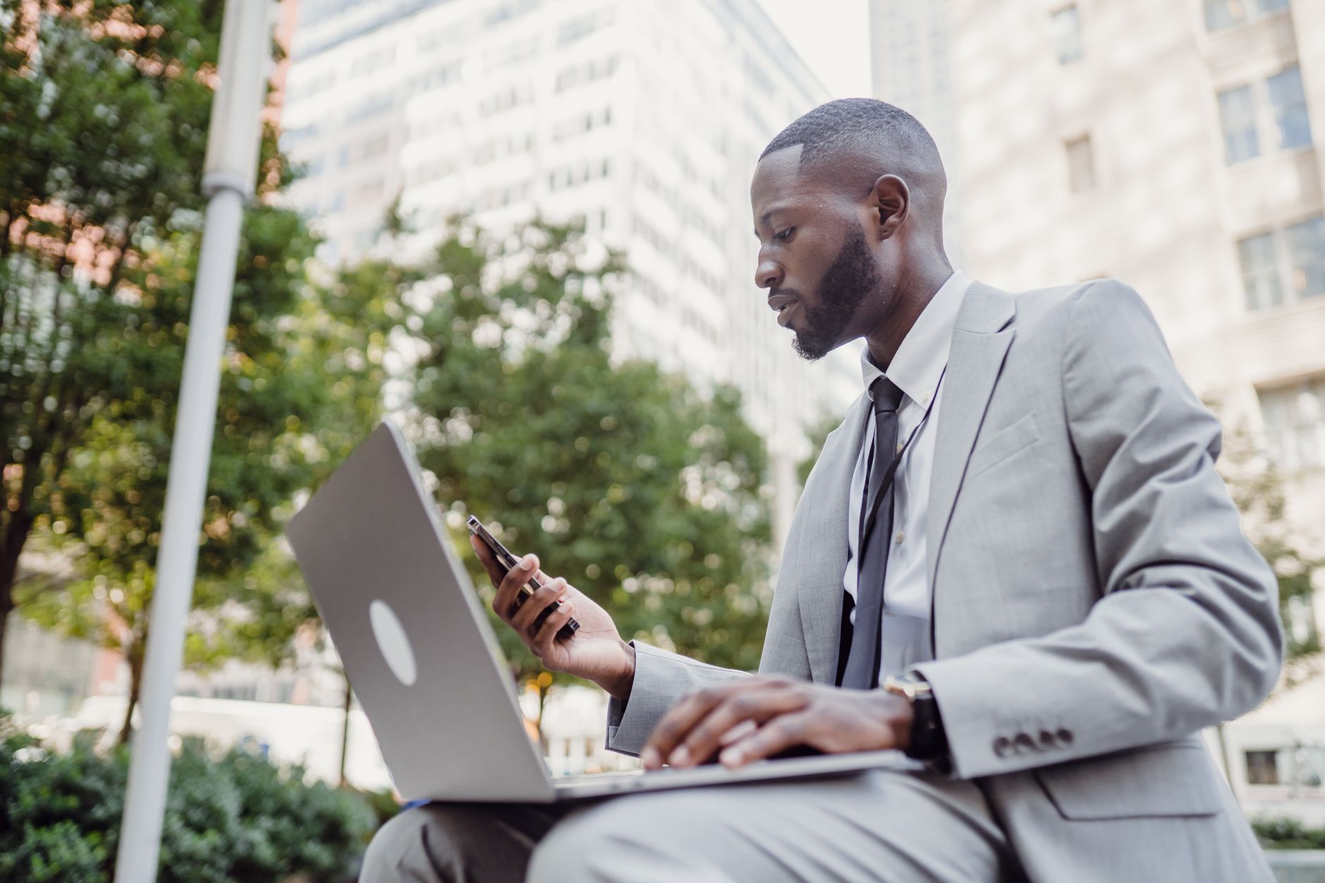 Businessman in a suit using a laptop and smartphone in an urban setting, blending technology with business. — Leon Harris: Aw