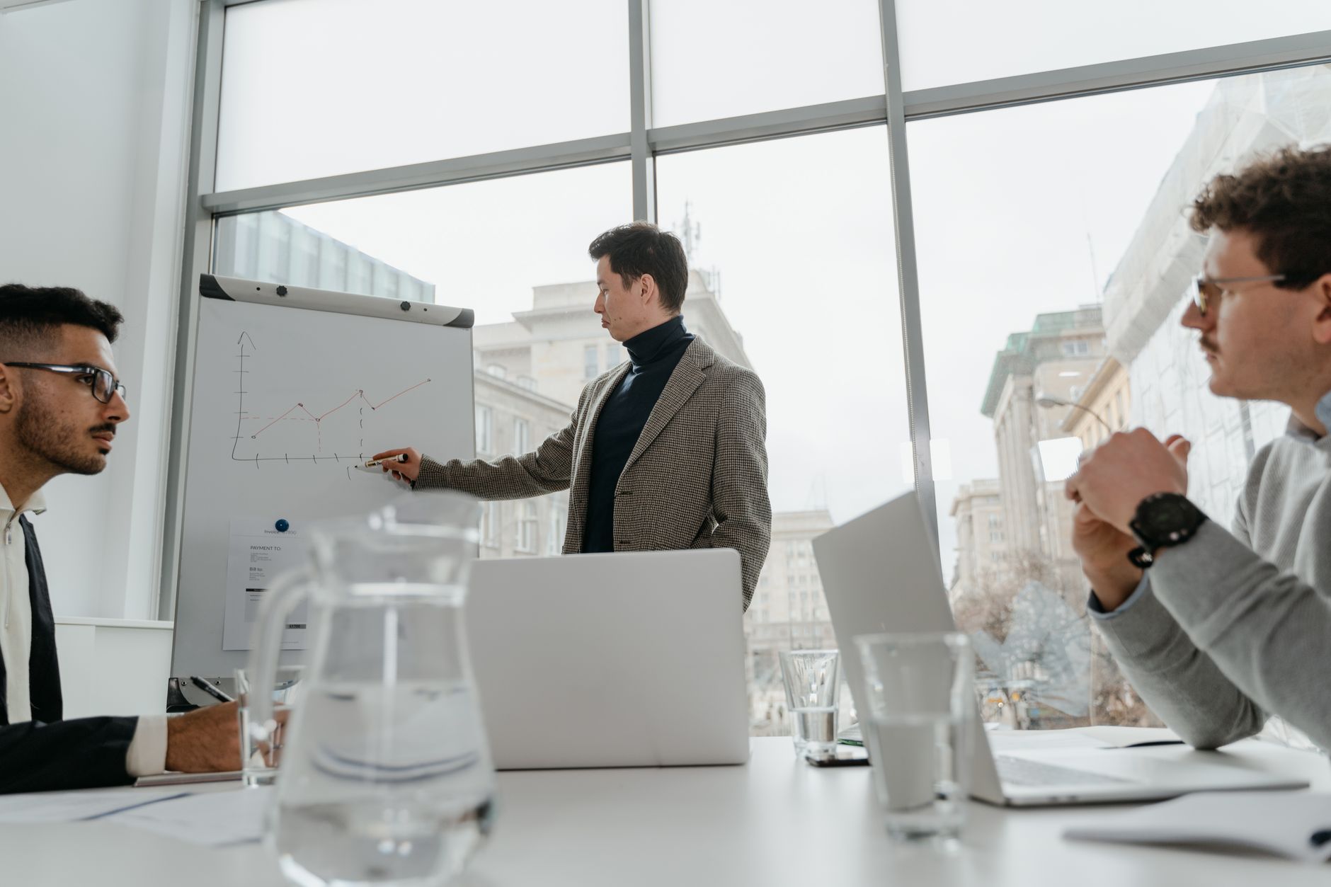 Professionals engaged in a collaborative business meeting with charts and laptops in a modern office setting. — Mastering Bus