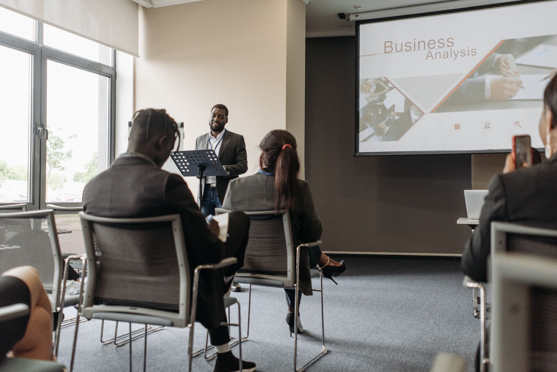 A business professional delivering a presentation in a conference room with diverse attendees. — Maxillofacial Surgery Myths