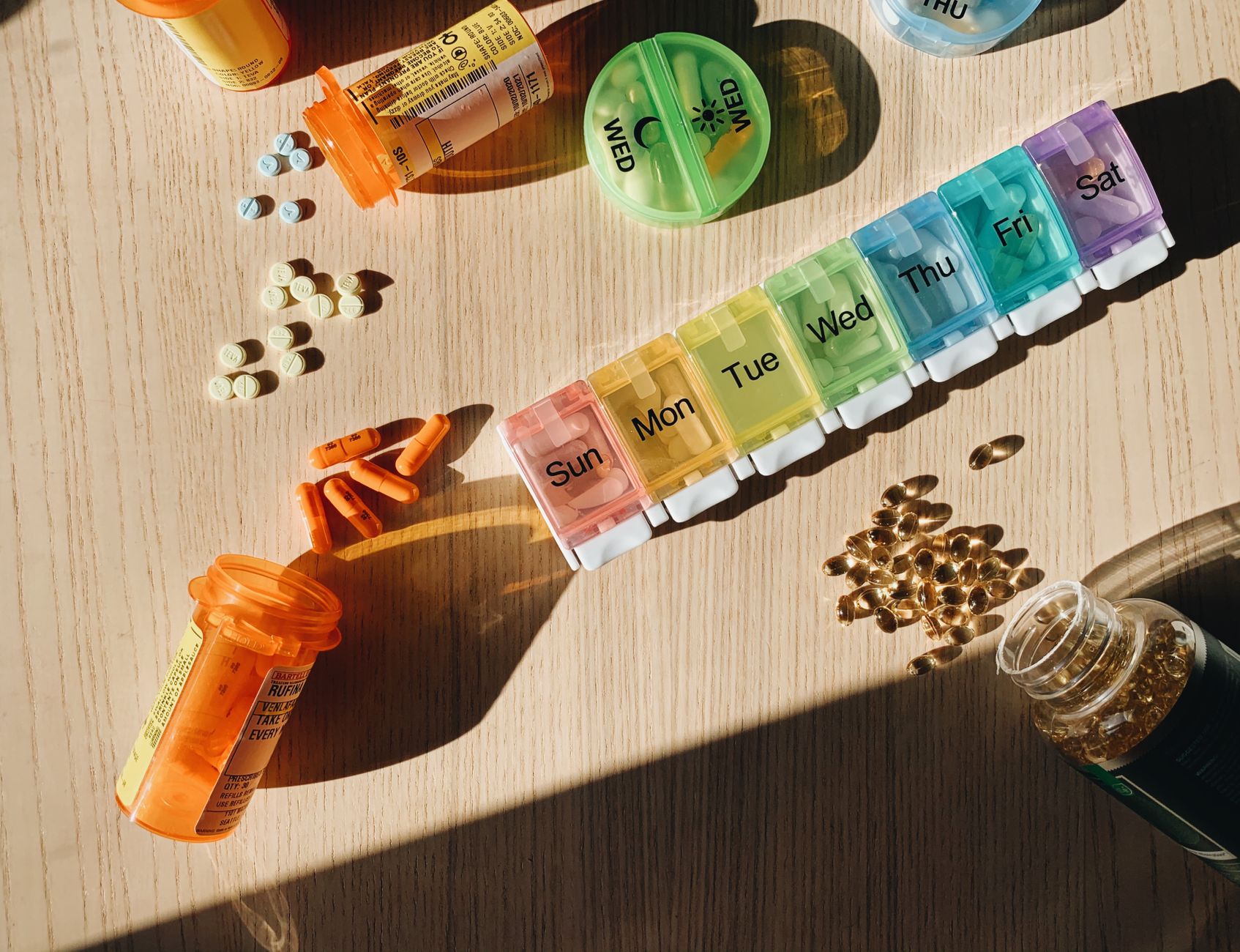 Colorful pill organizer with medication bottles and tablets on a wooden surface. — Nang Delivery Brisbane: Speedy and Conveni