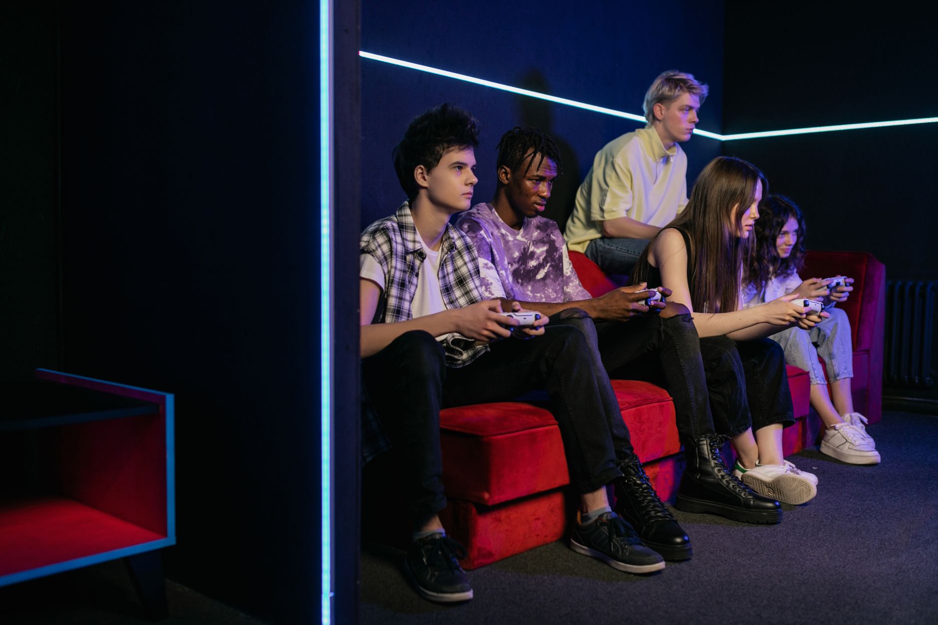 Teenagers enjoying video games together on a vibrant red couch in a modern gaming room. — Real-Time Results and Odds Come Sta