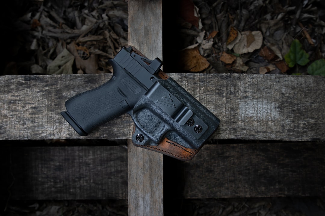 A handgun in a holster resting on wooden planks covered with leaves.
