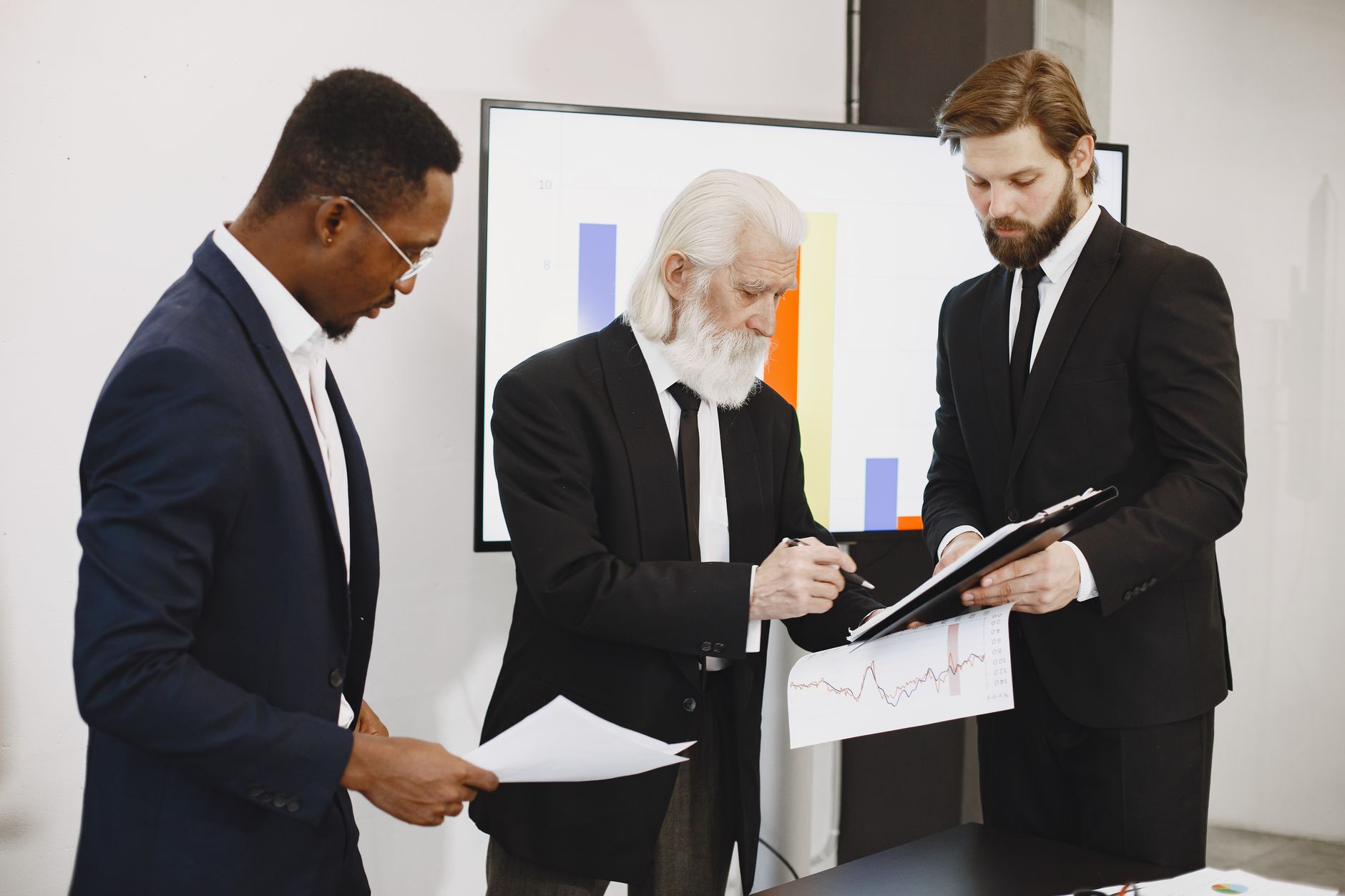 Three businessmen in suits reviewing reports and graphs during an office meeting. — The Untold Story of Nitun Ahir and the Li