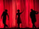 Silhouettes of performers on stage in front of a red curtain, depicting the art of storytelling through performance