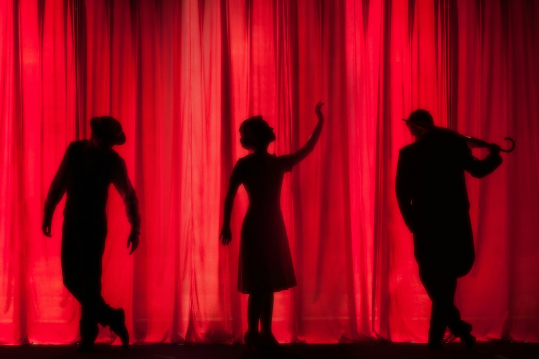 Silhouettes of performers on stage in front of a red curtain, depicting the art of storytelling through performance